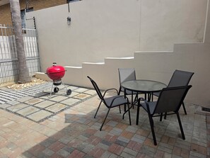 A patio with a round table and chairs, a red barbecue grill, and a tiled floor. - Perfect 2-bedroom apartment in a delightful Cape Town neighbourhood (Cape Town)