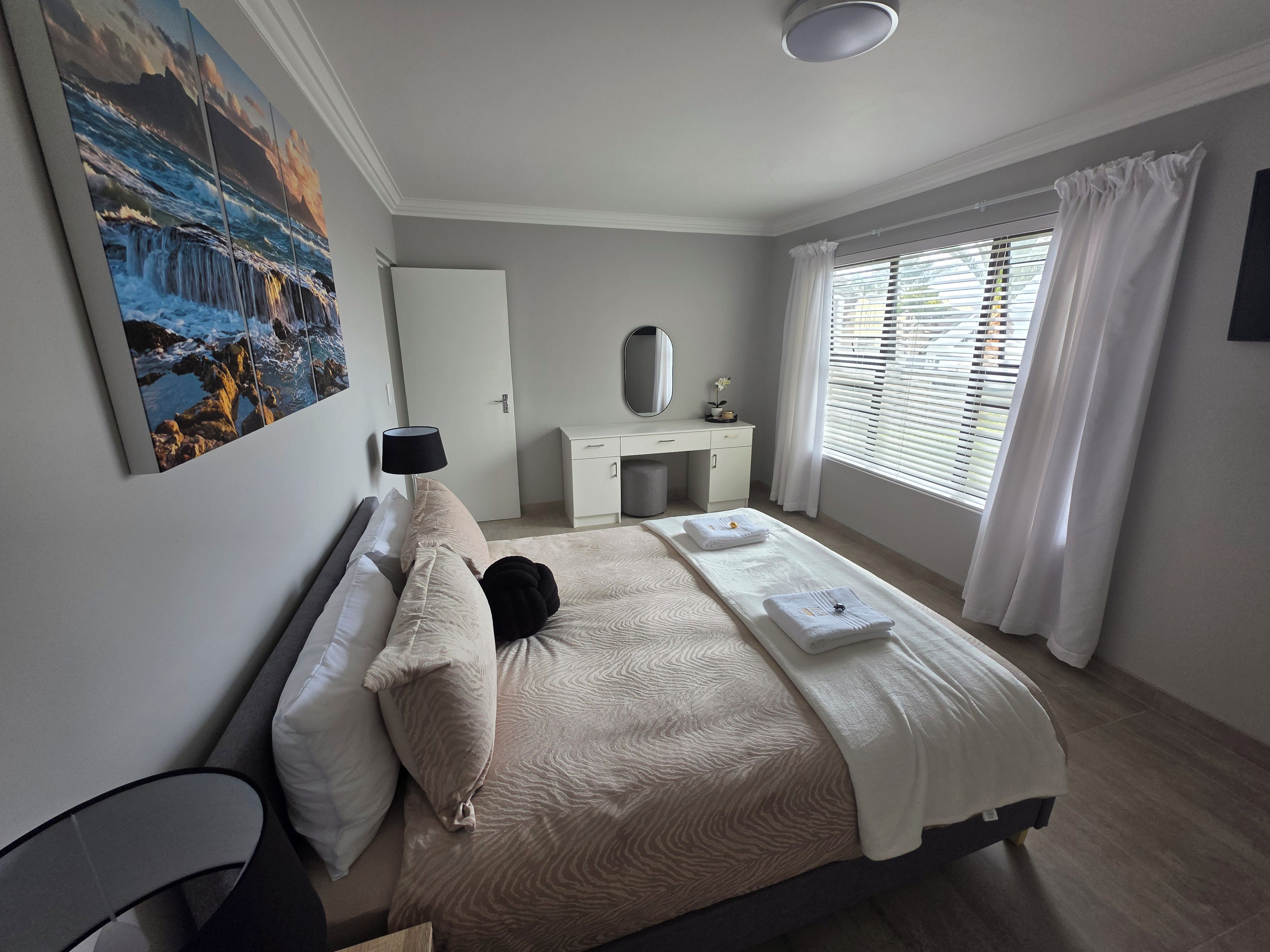 A bedroom with a bed, a desk, a chair, a window with blinds, and a painting on the wall.
