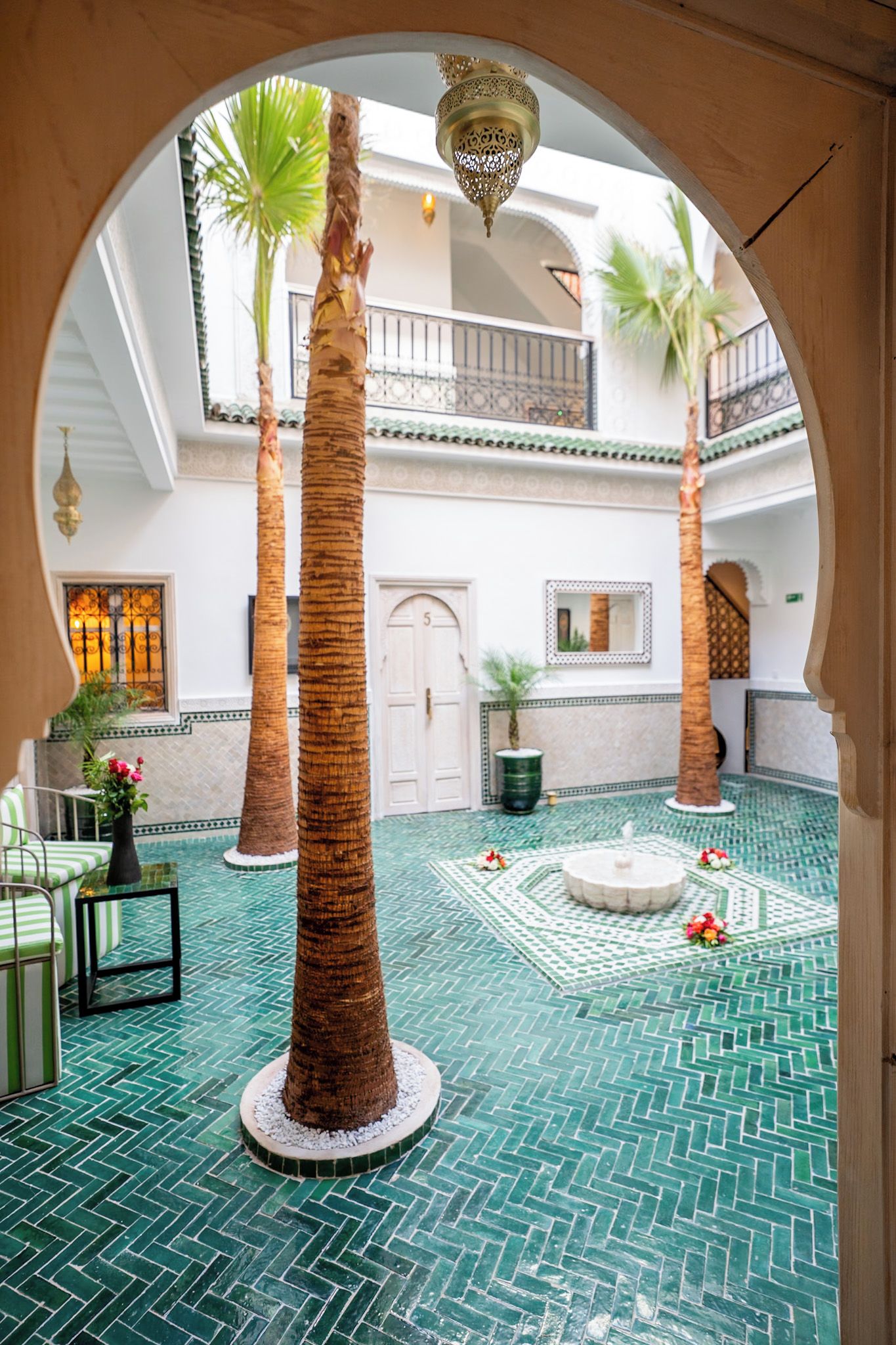 A courtyard with palm trees, a fountain, and a tiled floor.
