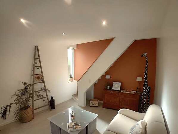 A modern living room with a staircase, a sofa, a coffee table, and a giraffe decoration. - Holiday Home “La Maison Tandem By Les Étapes” with Private Terrace and Wi-Fi (Chartres)