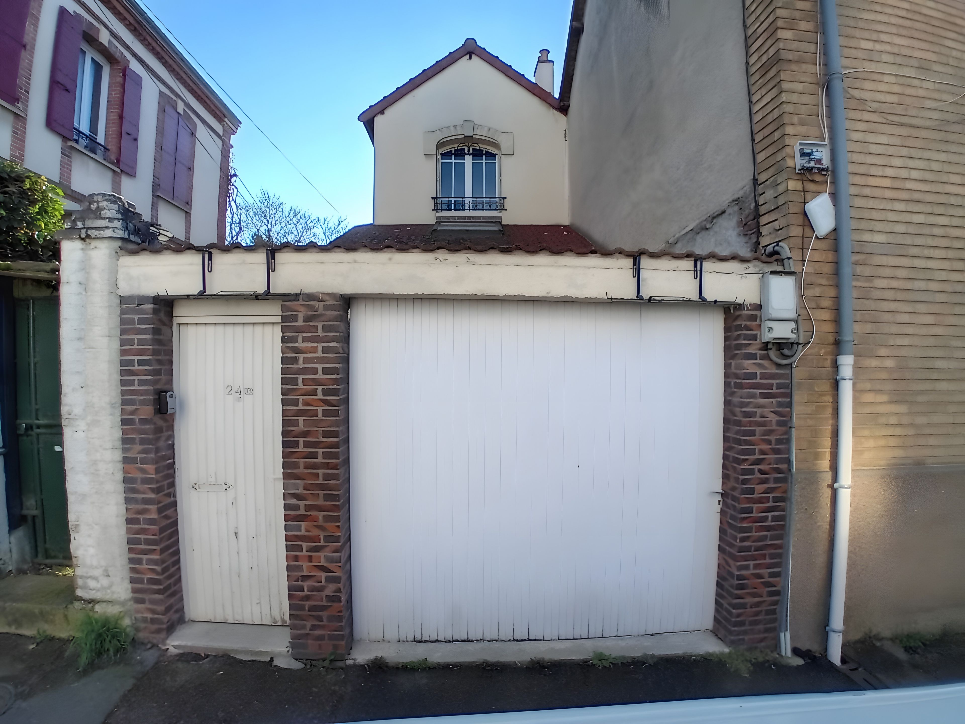 A building with a white garage door, brick walls, and a small balcony with a window.