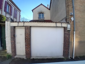 A building with a white garage door, brick walls, and a small balcony with a window. - Holiday Home “La Maison Tandem By Les Étapes” with Private Terrace and Wi-Fi (Chartres)