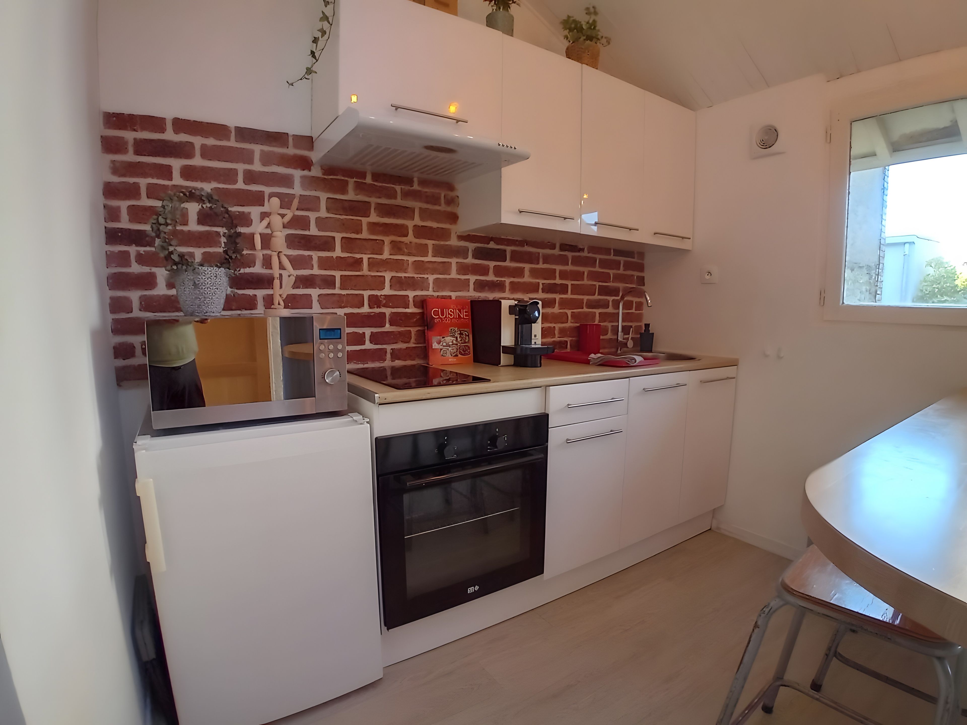 Kompakti keittiö, jossa on tiiliseinä, valkoiset kaapit, sisäänrakennettu uuni ja pieni työtaso.