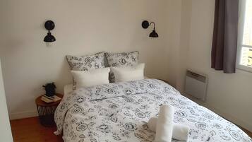 Une chambre à coucher avec un grand lit, deux lampes fixées au mur, un radiateur et une fenêtre avec des rideaux.