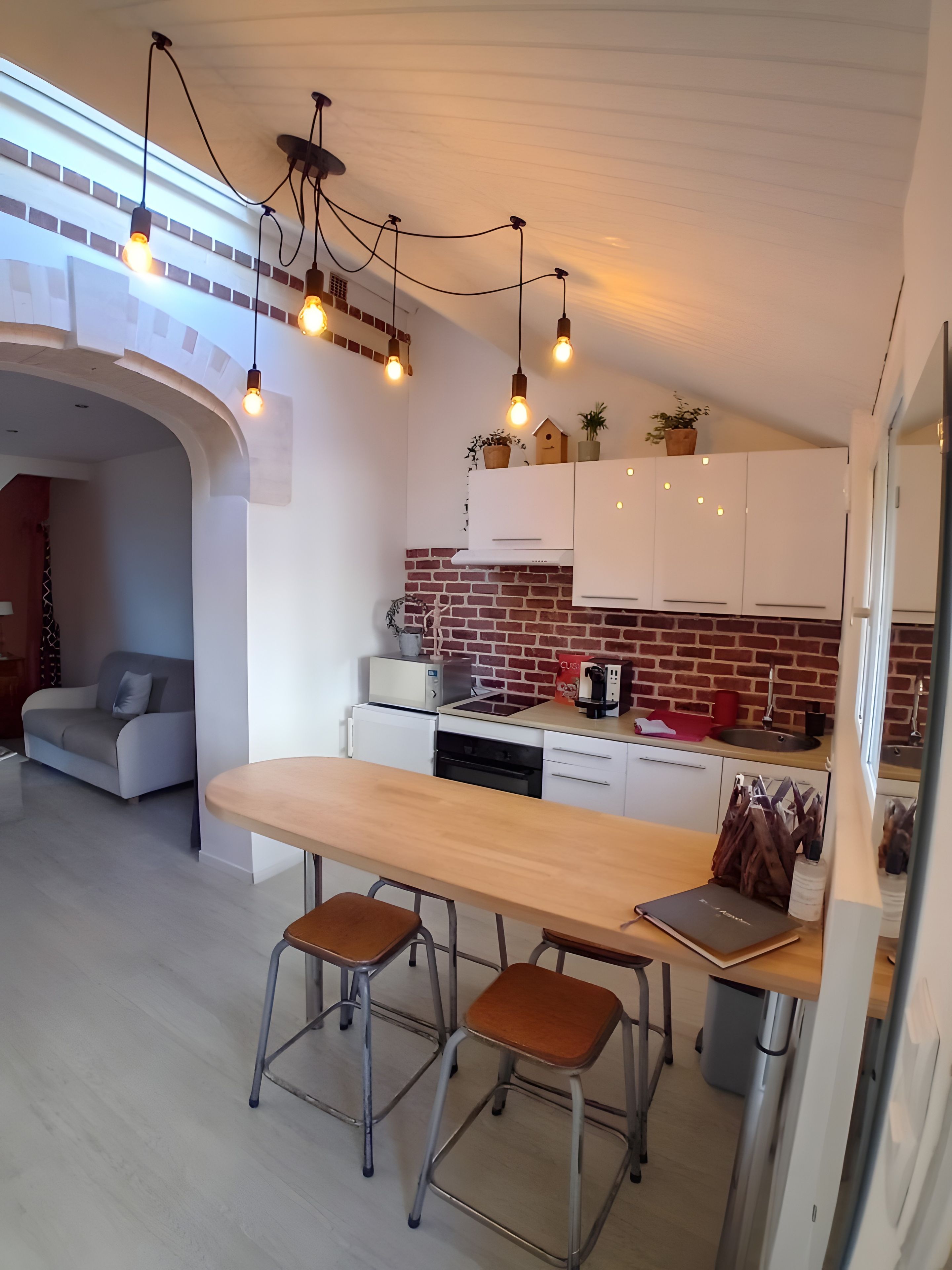 A modern kitchen with white cabinets, a brick backsplash, and pendant lighting.