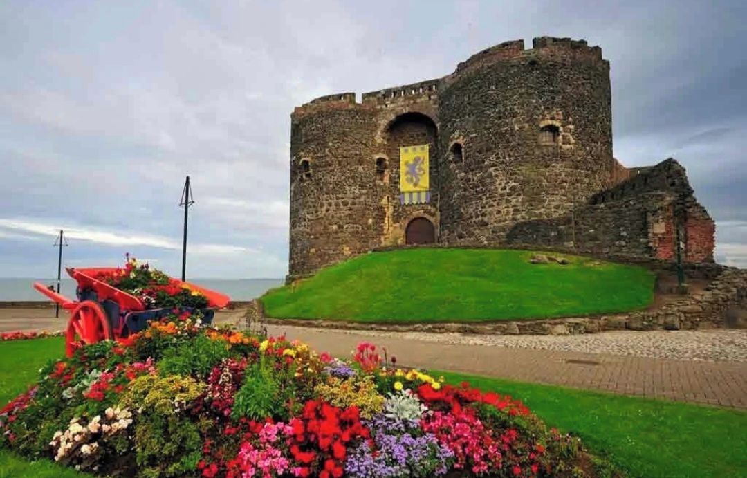A historic stone castle with a grassy foreground and a paved path leading to the entrance.