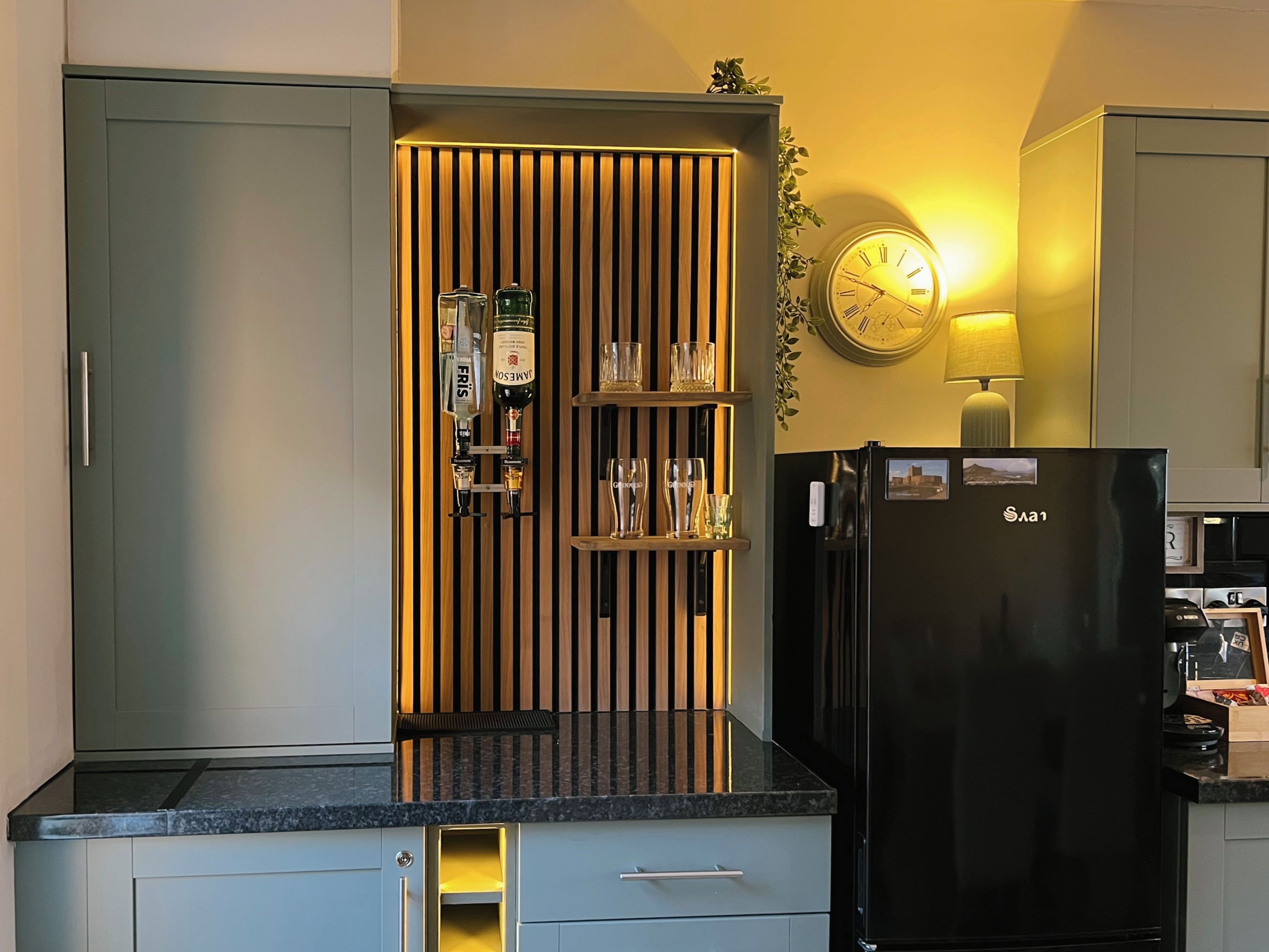 Una cocina con un refrigerador negro, revestimiento de madera en la pared y un reloj en la pared.
