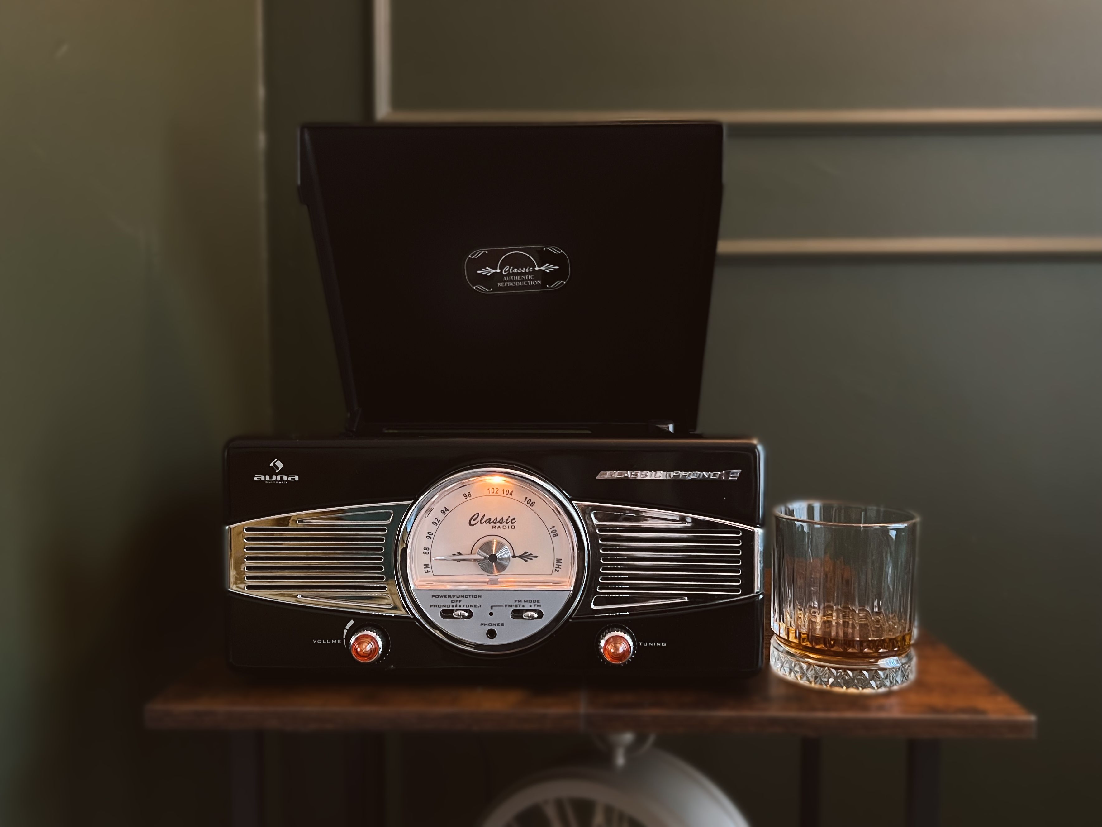 Une radio classique dotée de boutons de réglage du volume et de la fréquence, un verre de whisky et une table en bois.