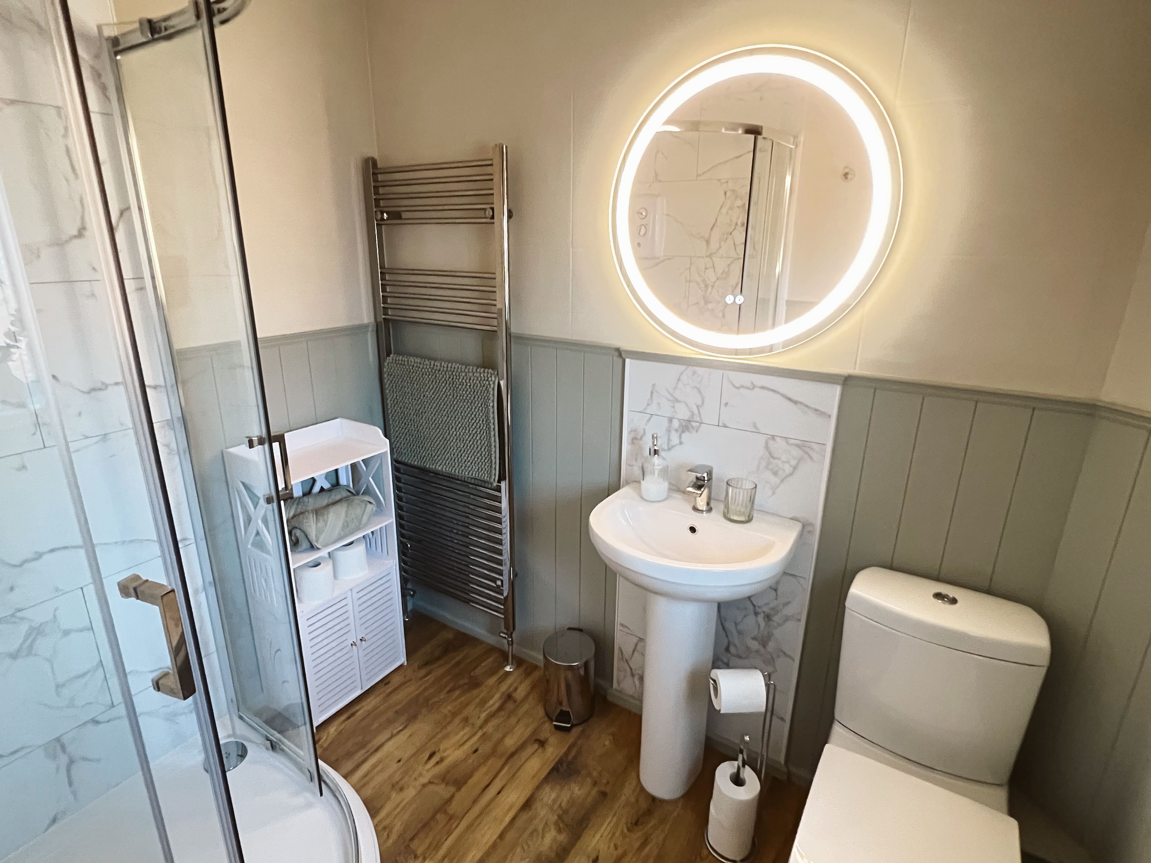 Ein Badezimmer mit Duschkabine aus Glas, einem weißen Waschbecken mit Marmorablage und einer Toilette.