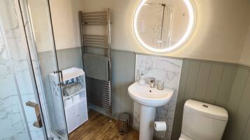 Ein Badezimmer mit Duschkabine aus Glas, einem weißen Waschbecken mit Marmorablage und einer Toilette.