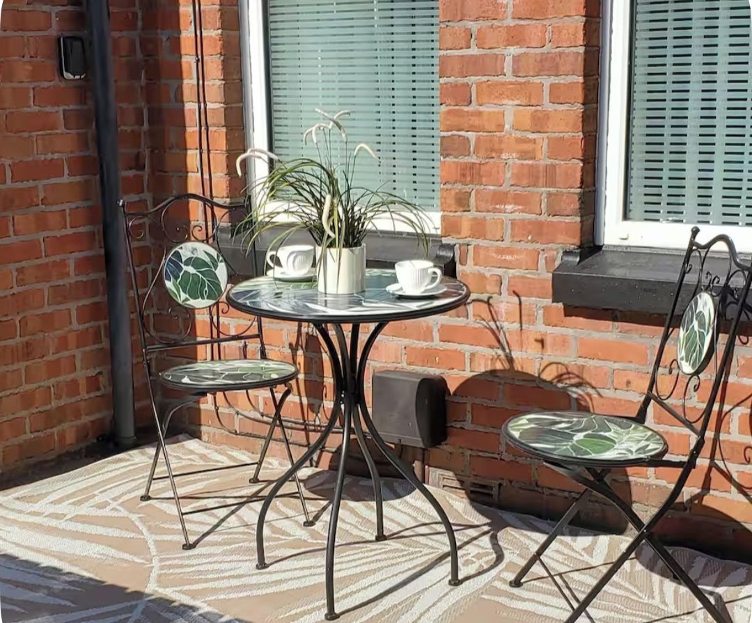 An outdoor seating area with a round table and four chairs, a potted plant, and a speaker.
