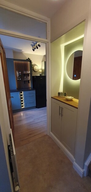 A hallway leading to a kitchen with a modern design, including a built-in oven and a wooden cabinet.