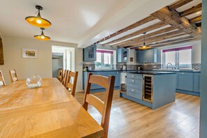 A modern kitchen with wooden beams, blue cabinets, and a dining area with a wooden table and chairs. - Host & Stay | Yeoman's House (Old Wives Lees)