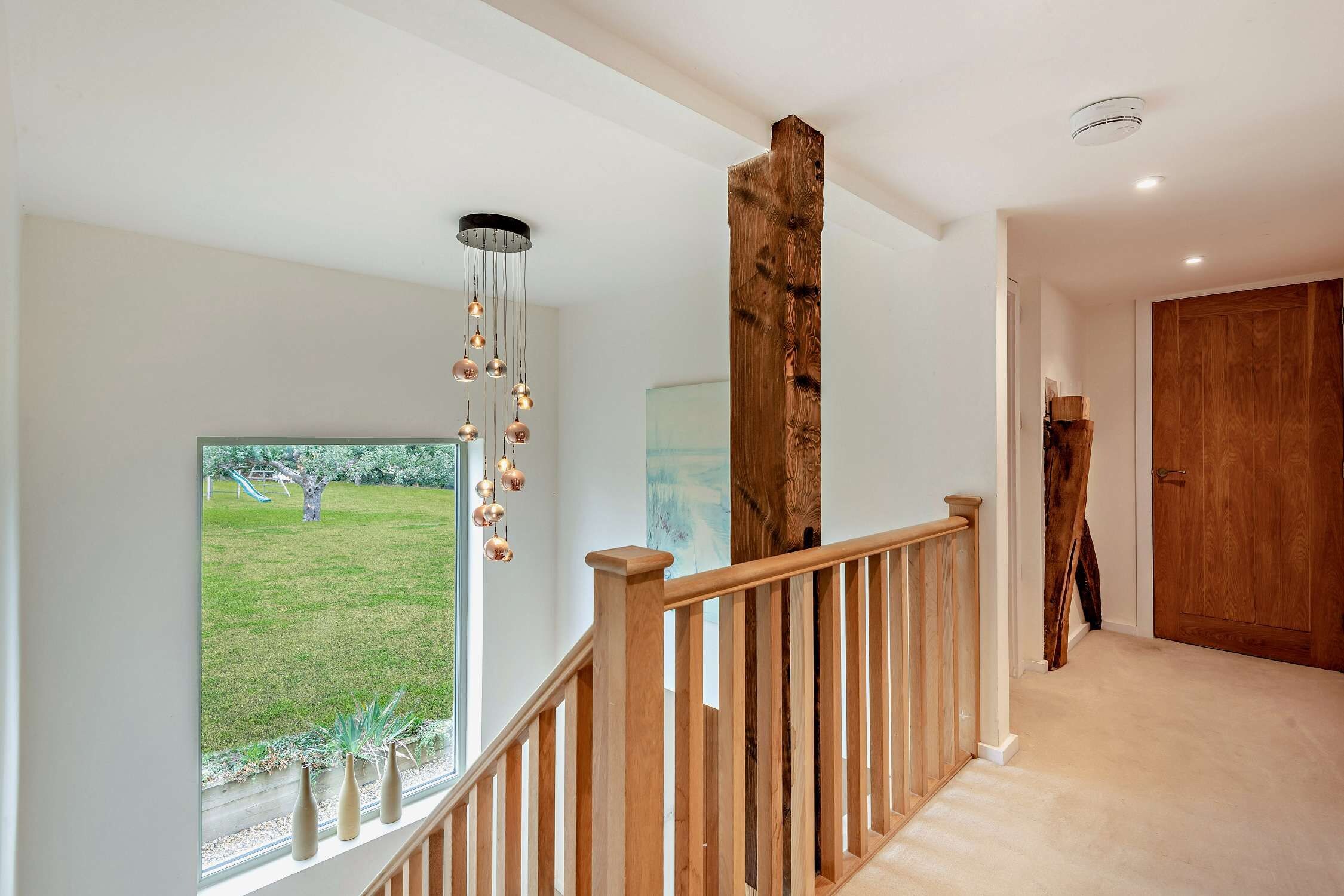 A modern interior with a wooden staircase, a view of a grassy area outside, and a wooden door.