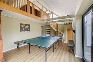 A spacious room with a ping pong table, wooden flooring, a world map on the wall, and a staircase leading to an upper level. - Host & Stay | Yeoman's House (Old Wives Lees)