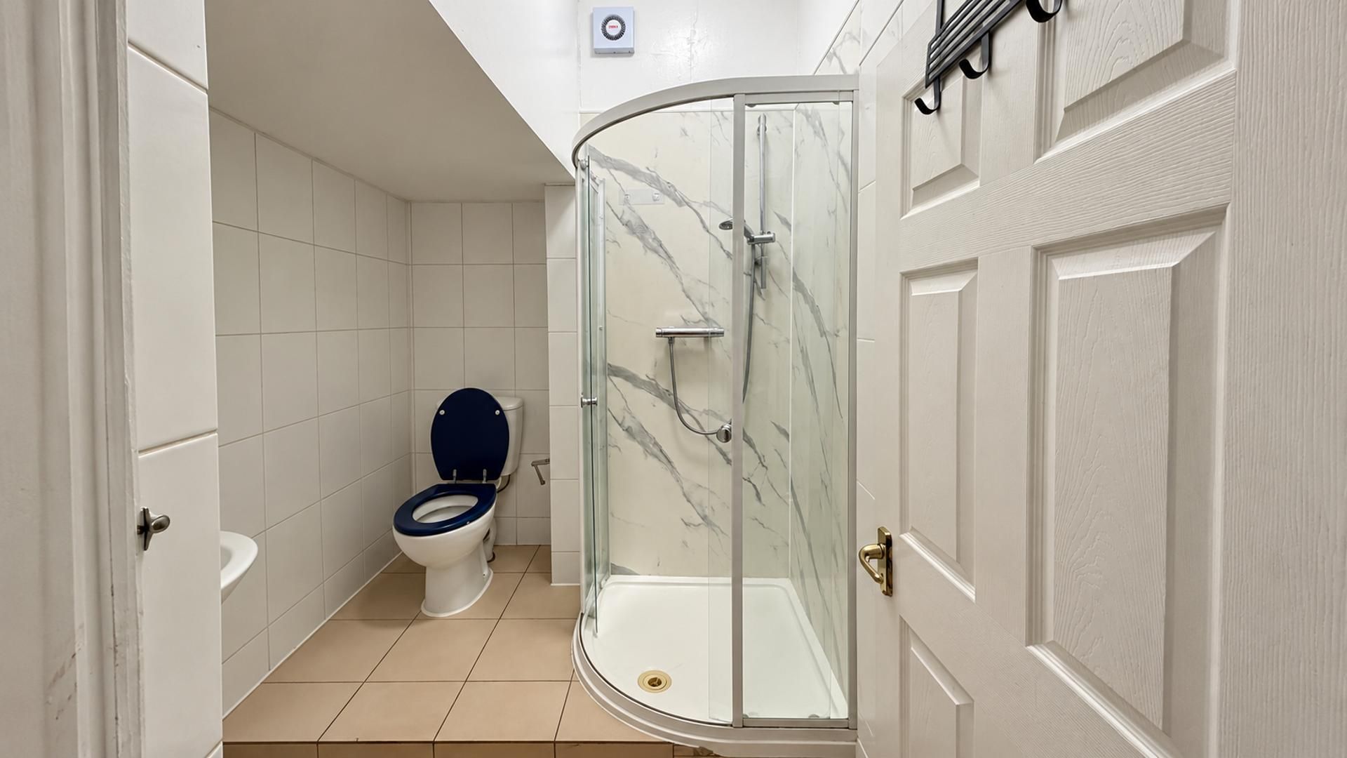 A bathroom with a glass-enclosed shower, a toilet with a dark blue seat, and white tiled walls.