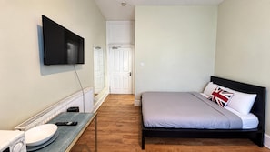 A bedroom with a bed, a television mounted on the wall, a small table with a sink, and a door leading to another room. - East London Studio, Sleeps 2 With Wifi (London)