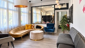 A modern living room with a sofa, ottoman, and armchair, a dining area with a table and chairs, and a large window with curtains. - East London Studio, Sleeps 2 With Wifi (London)