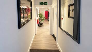 A hotel corridor with a fire exit sign, a red wall, and a plant.