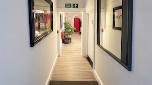 A hotel corridor with a fire exit sign, a red wall, and a plant. - East London Studio, Sleeps 2 With Wifi (London)