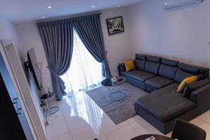 A modern living room with a grey sofa, a coffee table, and a rug. - 2-bedroom apartment in Loxwood House with AC, swimming pool and gym access (Accra)