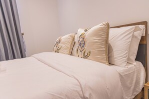 Ein Bett mit einem Holzkopfstück, einer beigen Bettdecke und zwei Kissen mit Blumenstickerei.