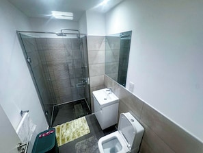 A compact bathroom with a glass shower enclosure, a white sink, and a toilet. - 2-bedroom apartment in Loxwood House with AC, swimming pool and gym access (Accra)
