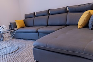 Ein Ecksofa mit vielen Kissen und ein kleiner Beistelltisch mit Fernbedienung.
