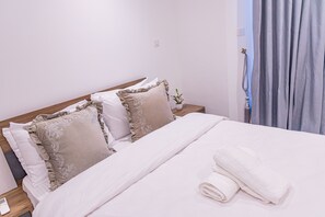 Un lit bien fait, avec des oreillers et une serviette enroulée, une table de chevet avec une lampe et une fenêtre avec des rideaux.