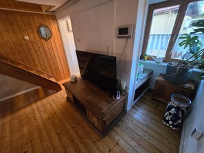 A room with wooden flooring, a fireplace, a small table with a television, and a window with a view.