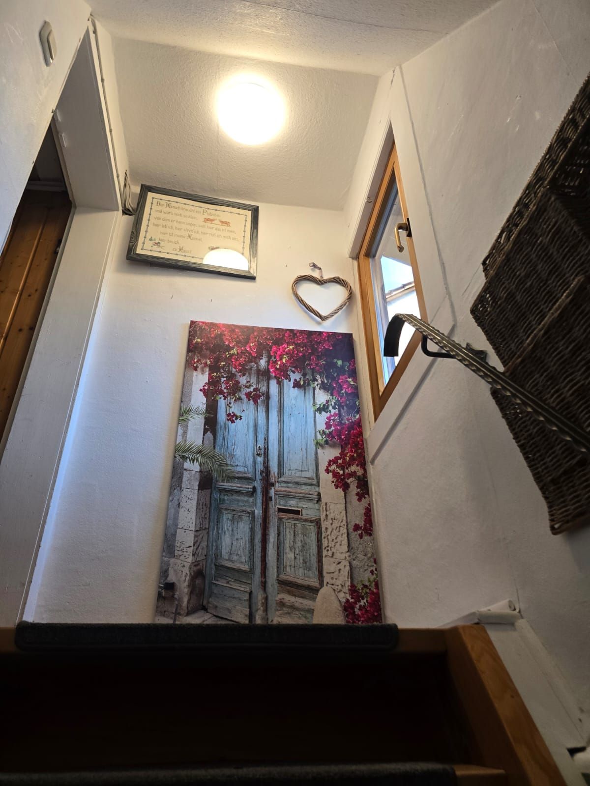 Eine Treppe mit einem gerahmten Zertifikat an der Wand, einer herzförmigen Dekoration und einem Gemälde einer Tür mit Blumen.
