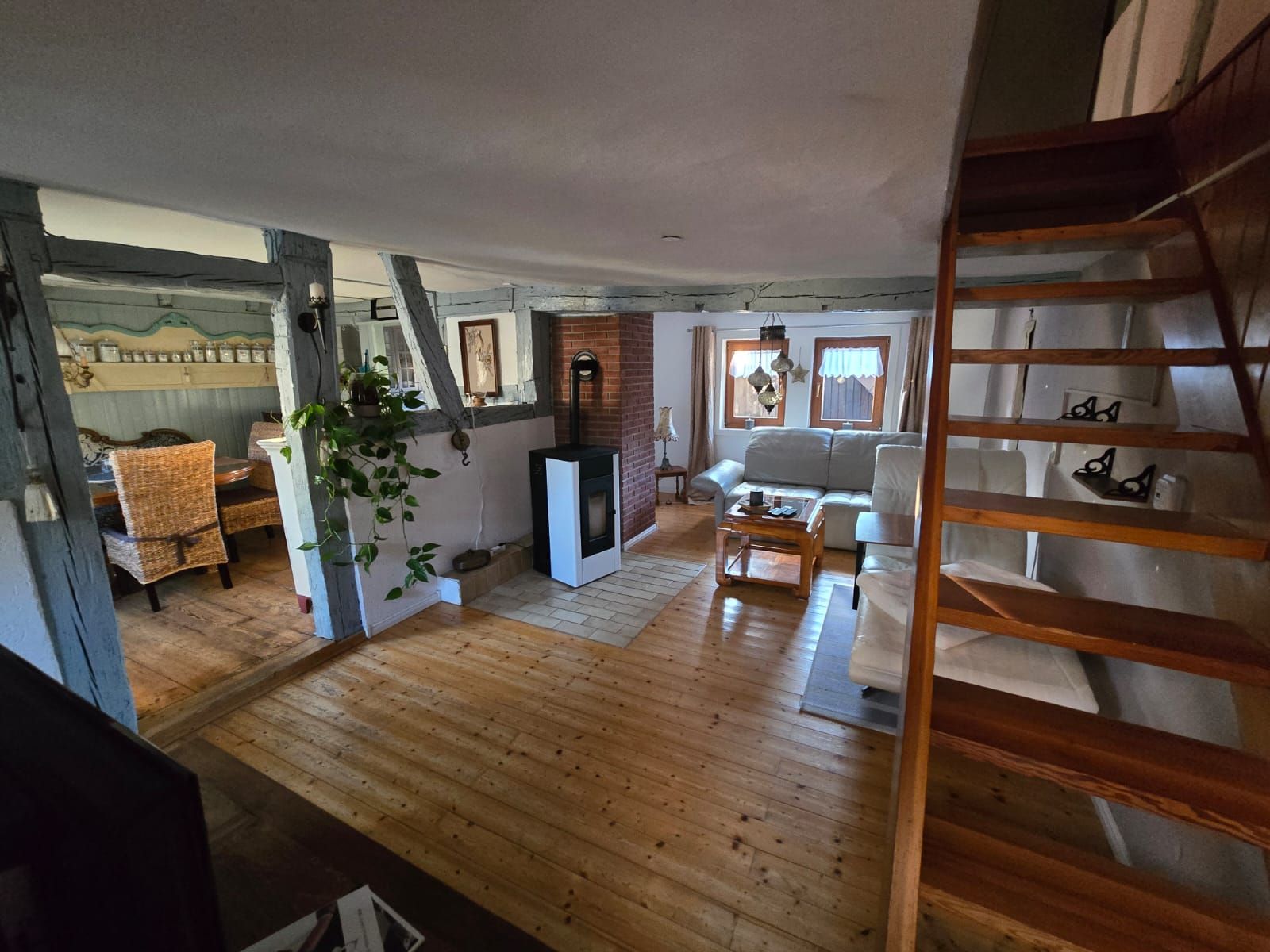 A cozy living room with a fireplace, wooden flooring, a sofa, and a dining area with wicker chairs.