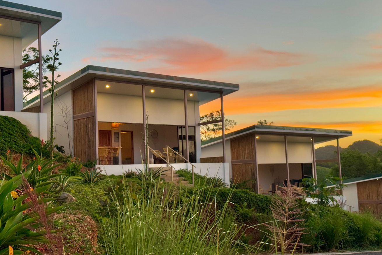 A modern two-story house with a covered outdoor area and a view of the sunset.