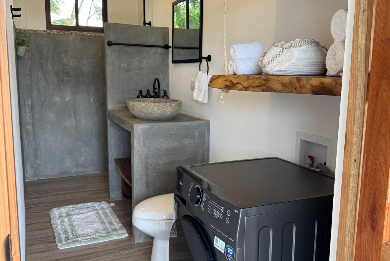 Un baño compacto con lavadora, un lavabo de piedra, inodoro y estante de madera con toallas.