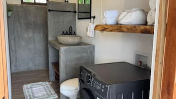 Un baño compacto con lavadora, un lavabo de piedra, inodoro y estante de madera con toallas.