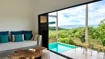 A modern living room with a large glass door leading to a balcony with a pool and outdoor furniture.