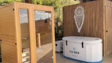 A sauna with a wooden exterior and glass doors, a white water tank, and a wooden cabinet with a decorative emblem.