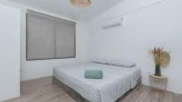 Un dormitorio con cama, mesita de noche, ventana y aire acondicionado de pared.