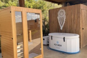 Een sauna met een houten gevel en glazen deuren, een witte wateropslag en een houten kast met een decoratief embleem.