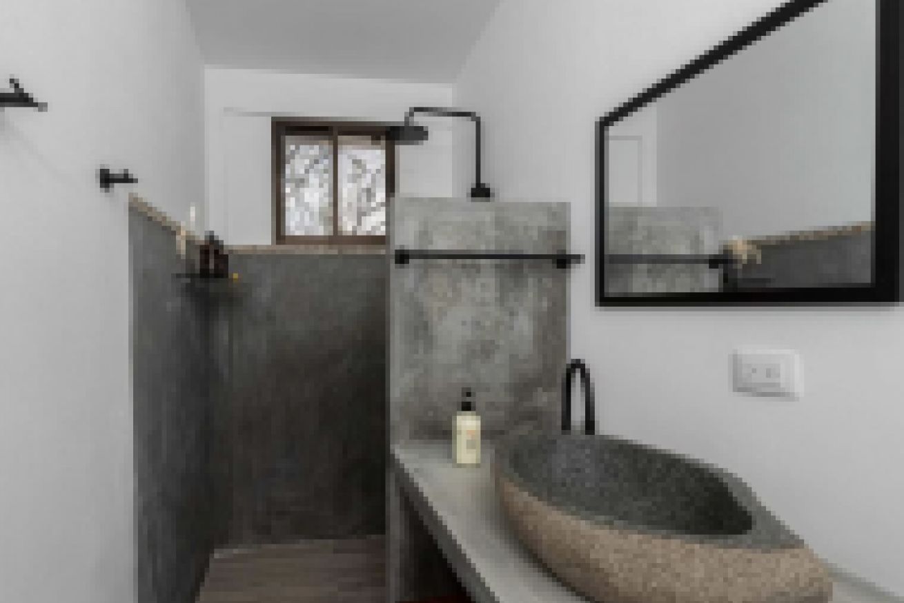 Un baño moderno con un lavamanos de piedra, un espejo y una ducha.