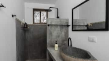 Un baño moderno con un lavamanos de piedra, un espejo y una ducha.