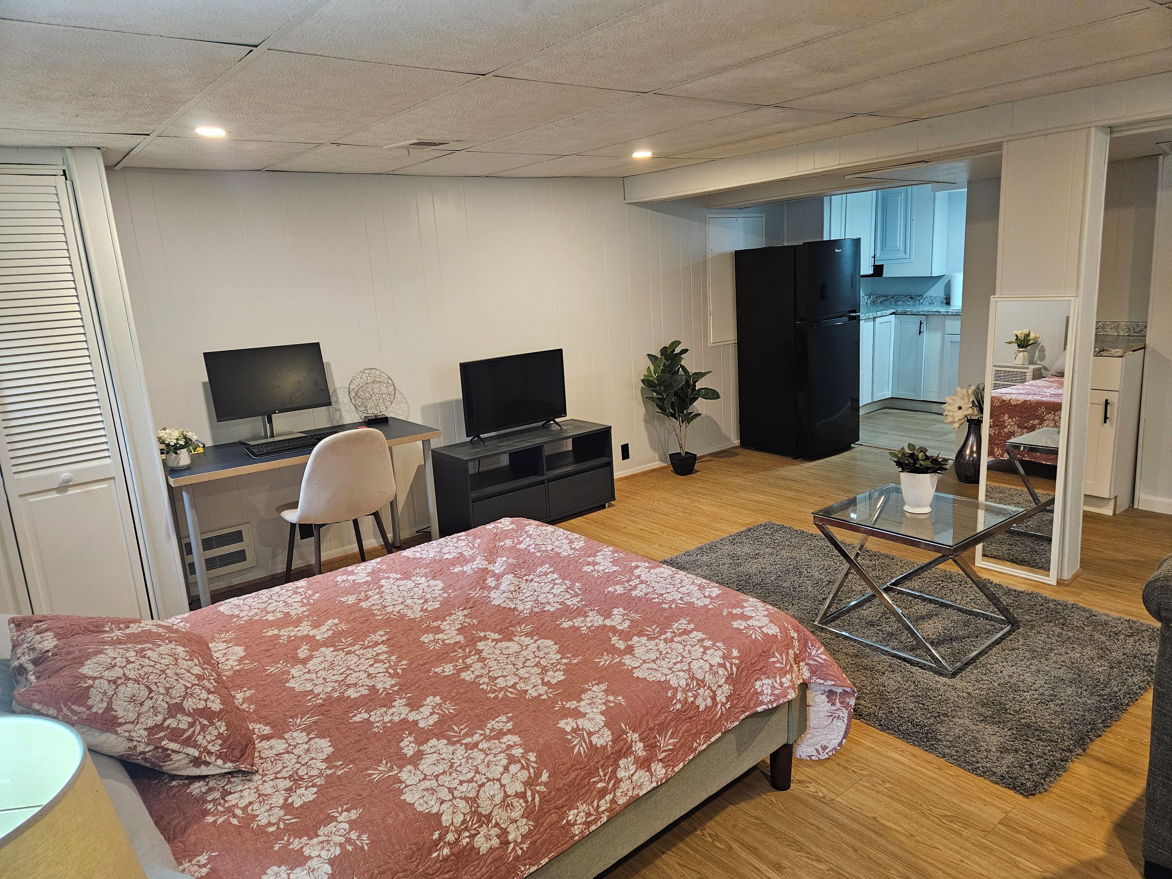 A bedroom with a bed, a desk with a computer, a television, and a refrigerator.