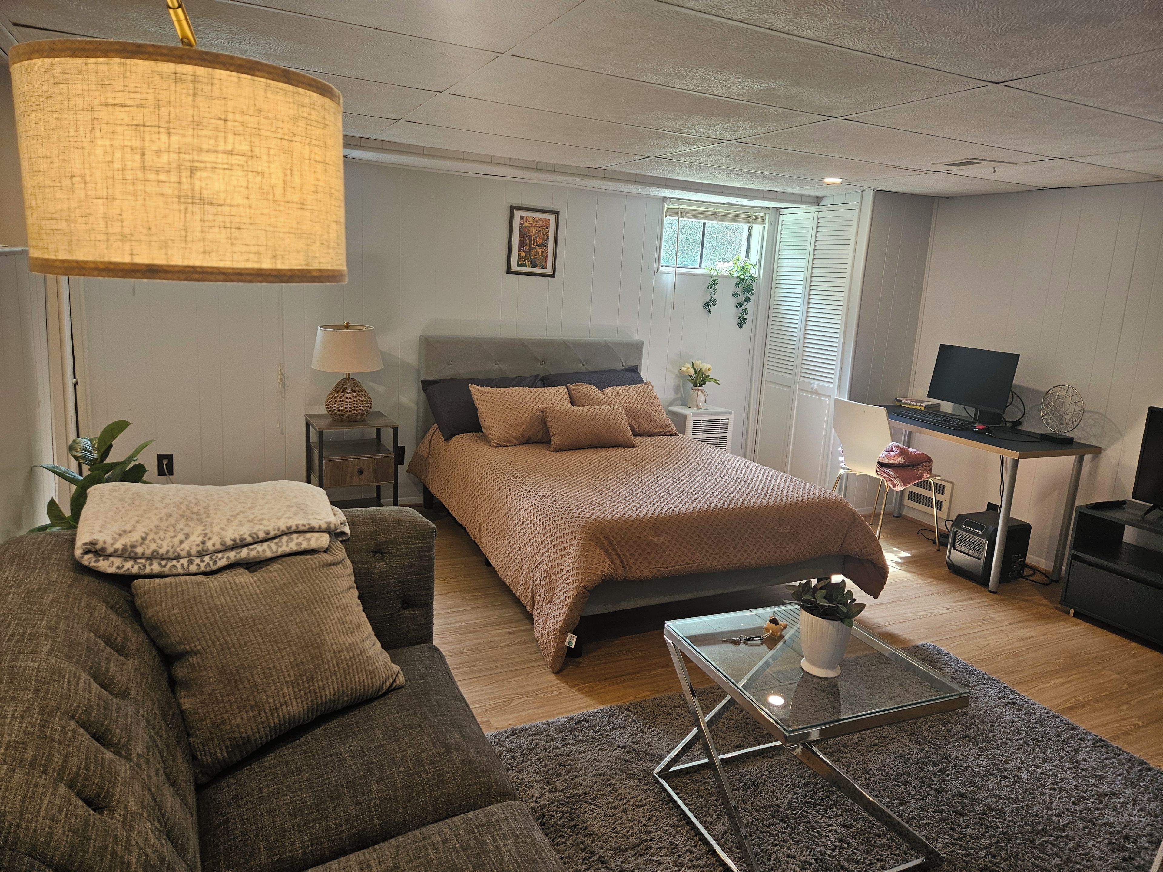 A modern bedroom with a bed, bedside tables, a desk, and a computer setup.