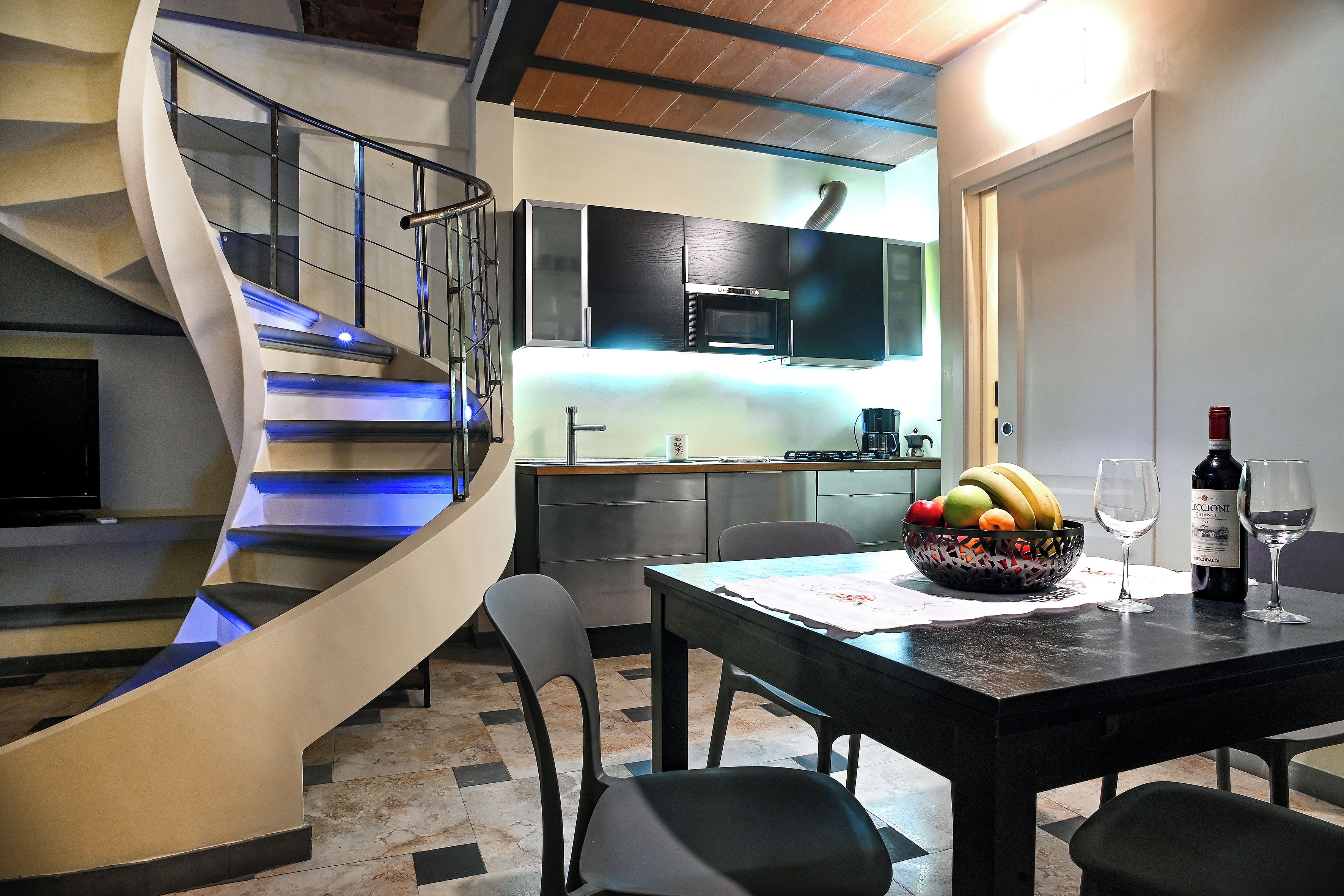 Une cuisine moderne dotée d’un four encastré, d’une table à manger avec des chaises et d’un escalier en colimaçon.