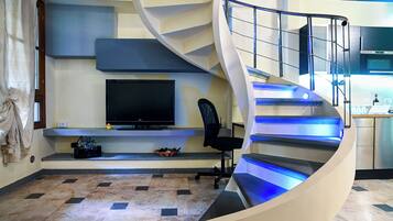Un intérieur moderne avec un escalier à volutes, un téléviseur à écran plat, un fauteuil de bureau noir et un coin cuisine.