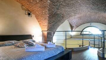 A bedroom with a high, arched ceiling, a bed with patterned bedding, and a view of a circular skylight.