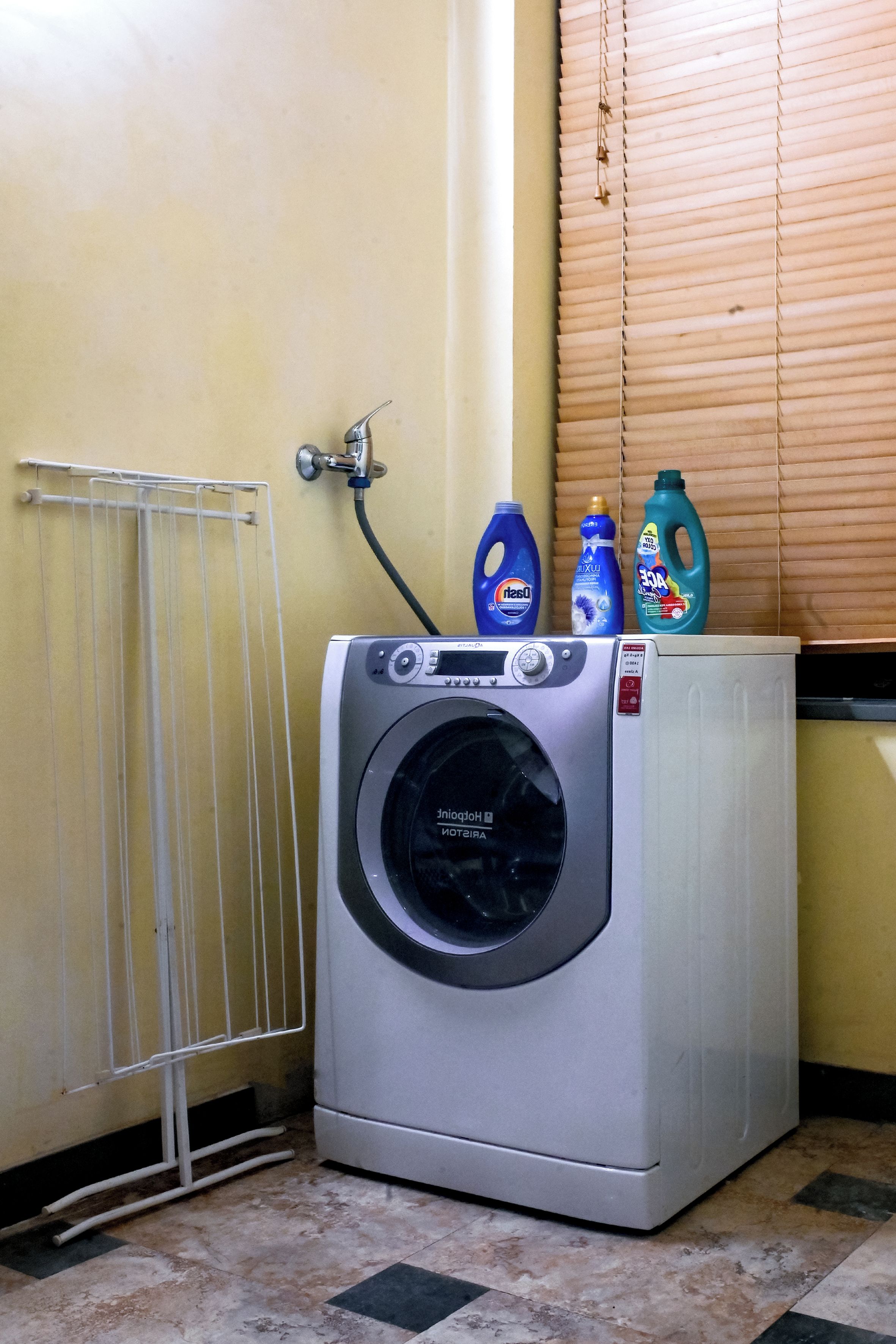 Une machine à laver compacte, de couleur argentée, à chargement frontal, dotée d’un panneau de commande, d’un tuyau et de deux bouteilles de détergent placés sur le dessus.