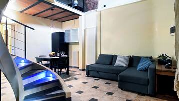 A modern living room with a sofa, a dining table, and a staircase with blue lighting.