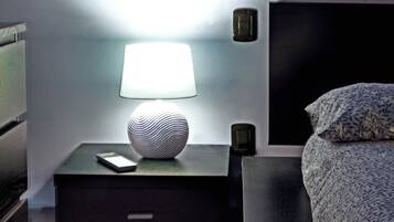 A neatly arranged hotel room with a bedside table, a lamp, a decorative vase, a remote control, and a patterned bedspread.