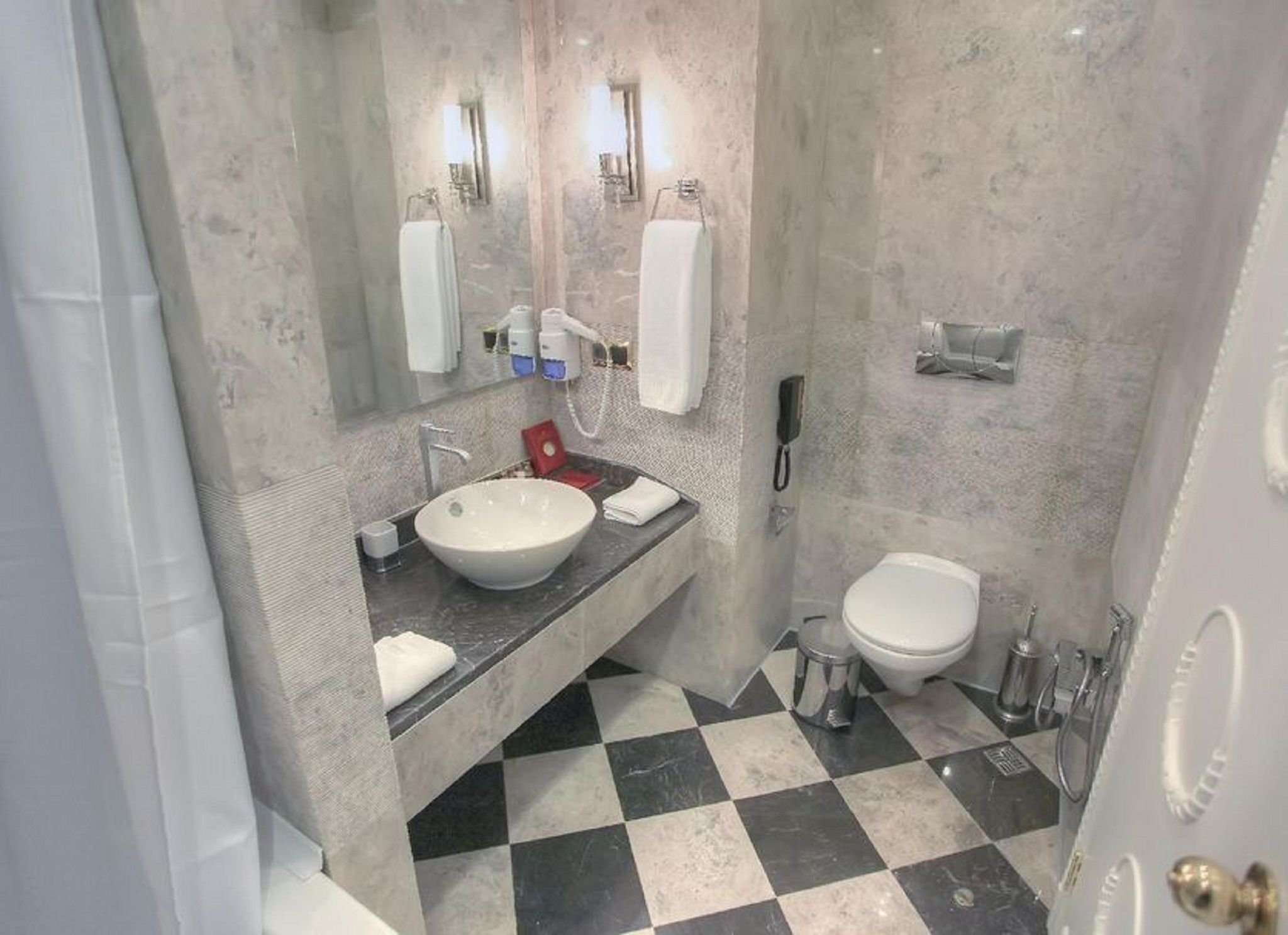 A bathroom with a large mirror, a sink, a toilet, and a checkered floor.